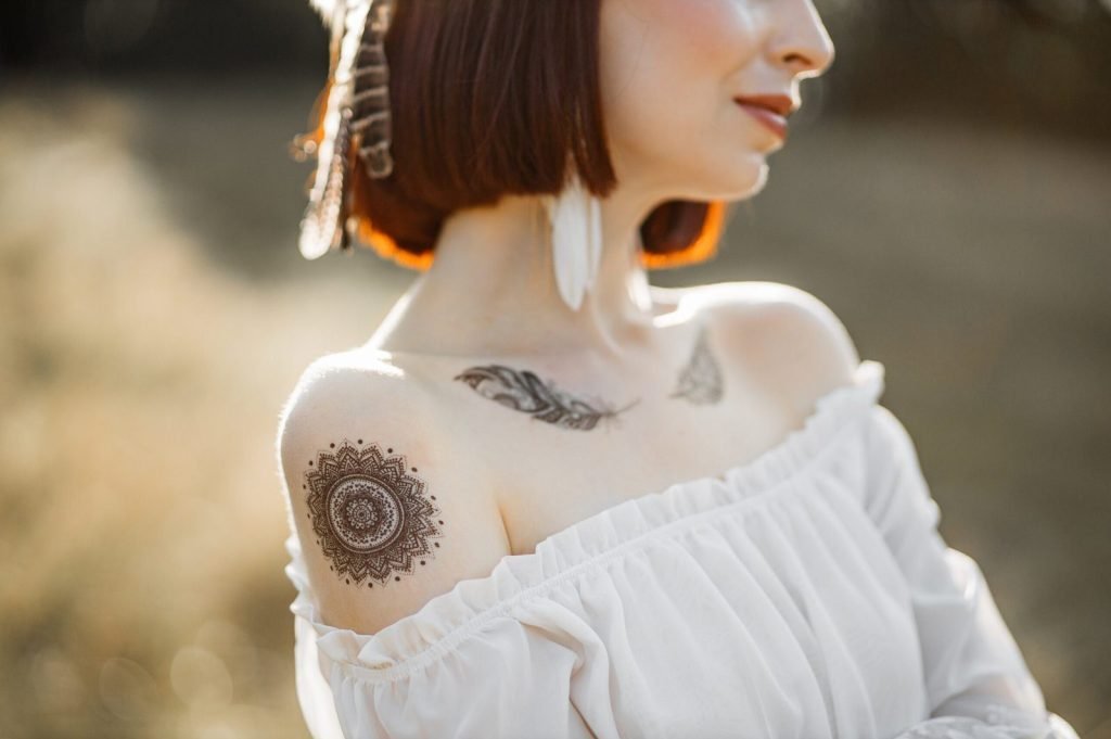 Close up native American woman neckline portrait. Cropped shot of pretty charming indian woman in white dress with bare shoulders, feather jewerly and body art tattoos, in the nature